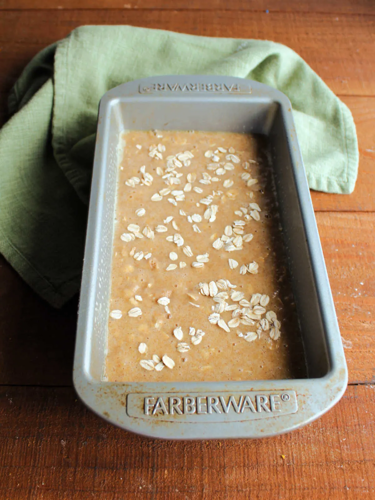 Applesauce oatmeal quick bread batter in loaf pan topped with extra oats, ready to go in the oven.