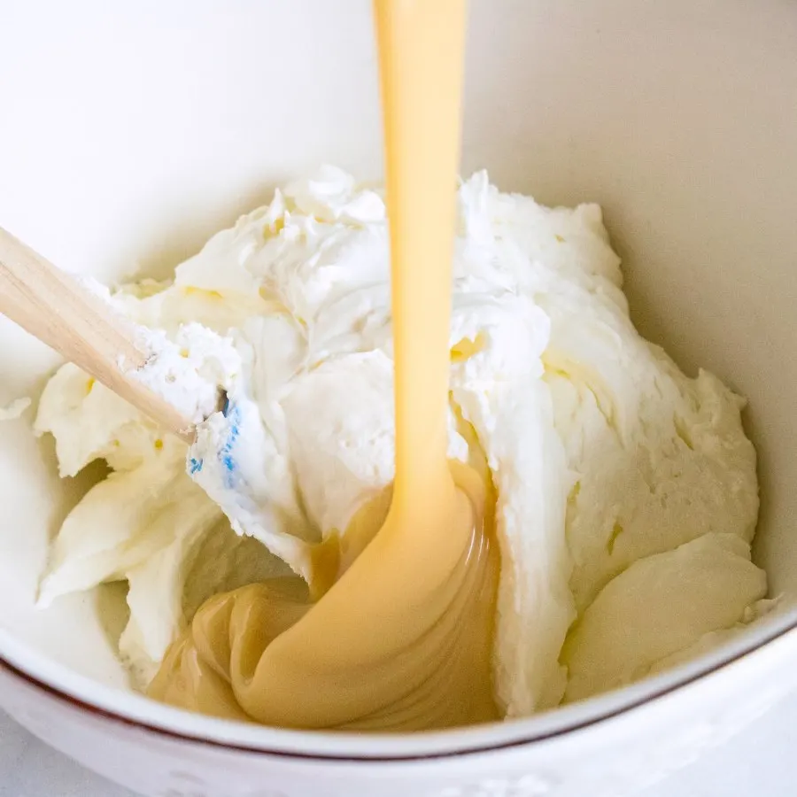 pouring sweetened condensed milk over bowl of whipped cream.