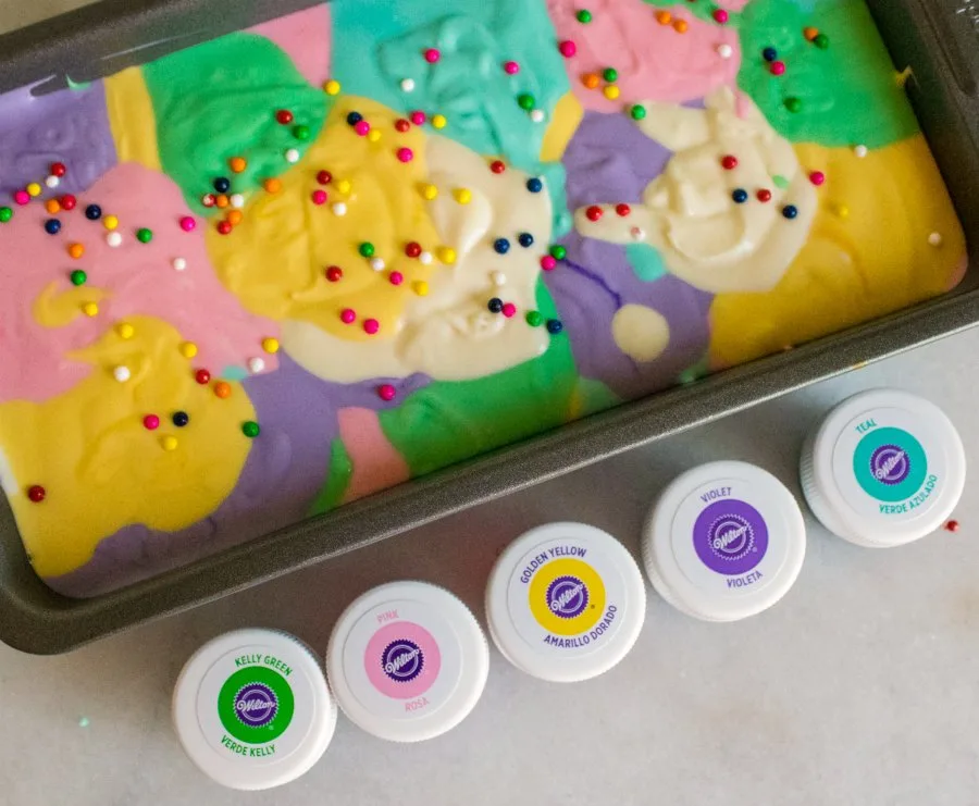 dollops of different colors of ice cream base in loaf pan with bottles of gel food coloring nearby.