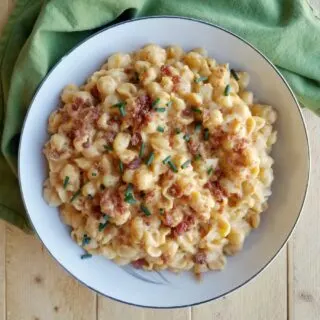 Bowl of pumpkin macaroni and cheese topped with crumbled bacon and chives.
