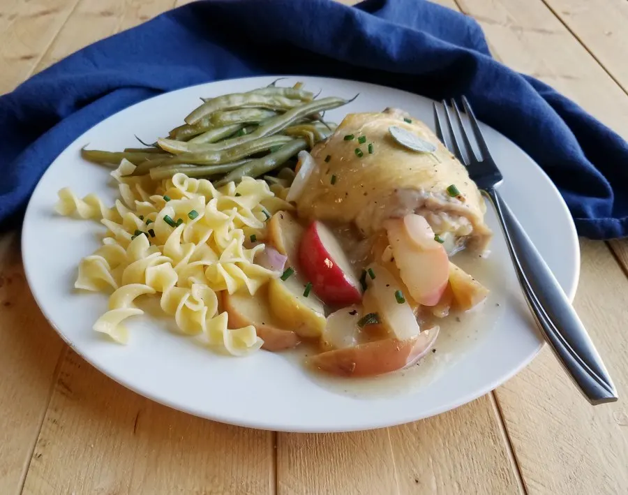 dinner plate with chicken and apples, buttered noodles and green beans, side view.
