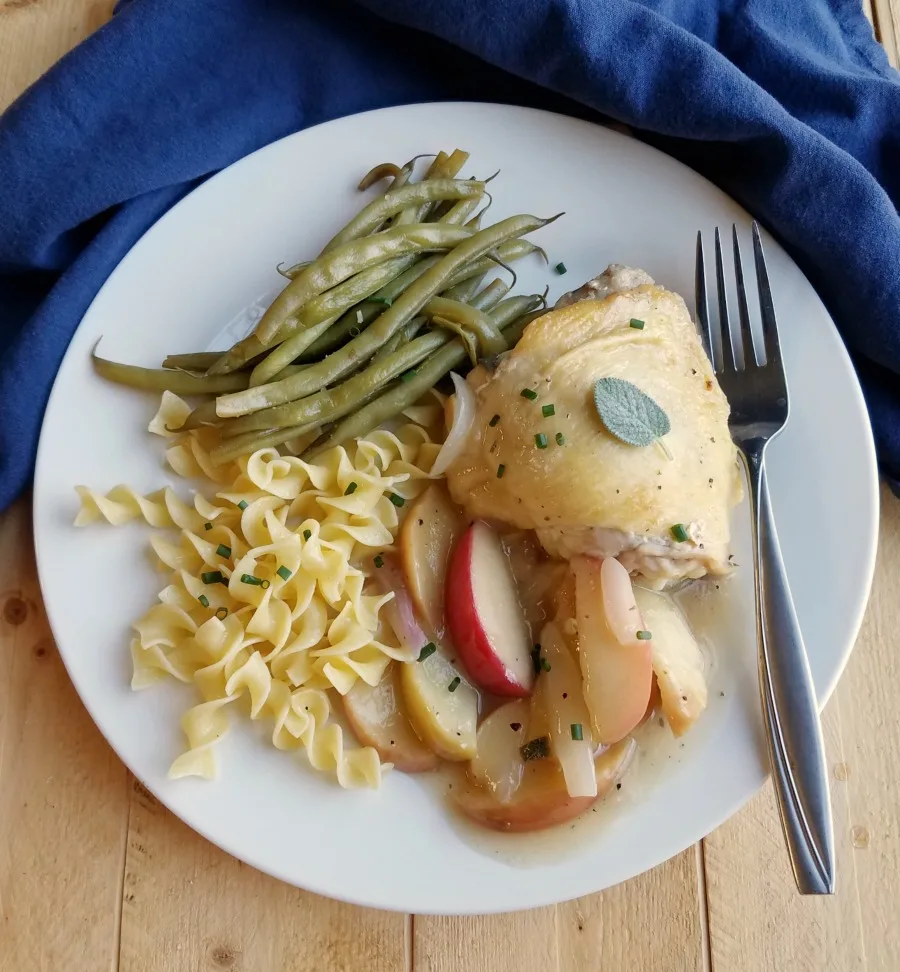Dinner plate with chicken thigh and cooked apples, buttered noodles, and roasted green beans, ready to eat.