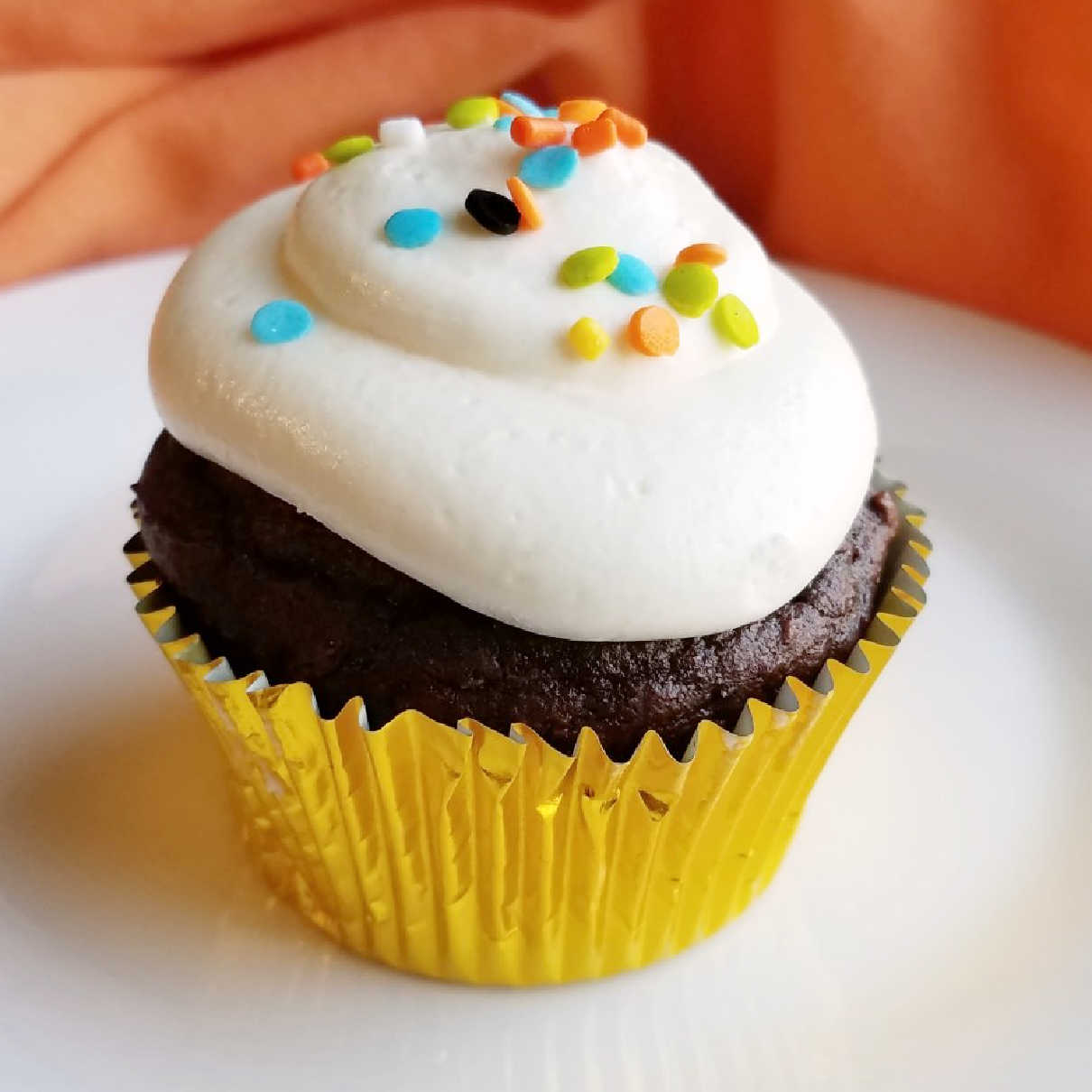 close up of chocolate pumpkin cupcake with frosting and sprinkles.