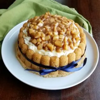 cinnamon charlotte cake filled with cream cheese whipped cream and caramel apple topping with a blue ribbon tied around the outside