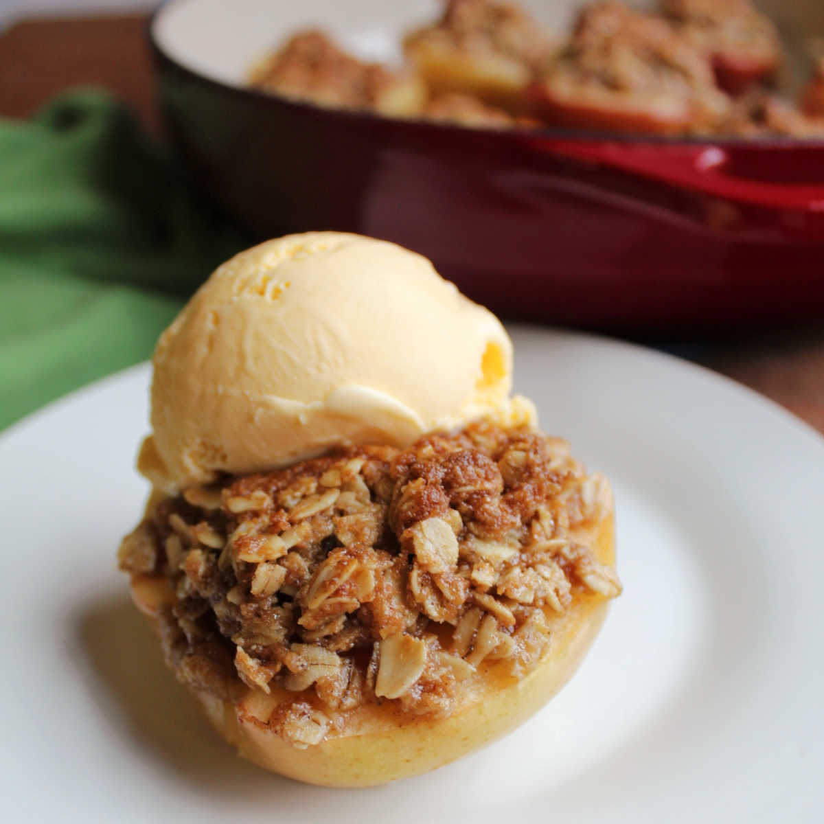 Baked apple half stuffed with brown sugar and oat crisp topping finished with a scoop of vanilla ice cream, ready to eat.