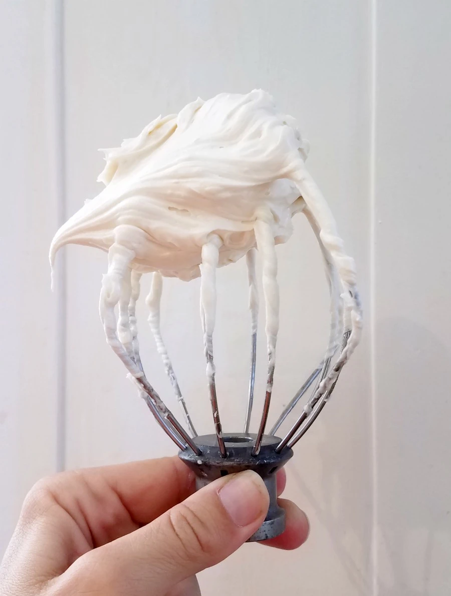 mixer whisk held upside down with a swirl of white whipped sweetened condensed milk frosting.