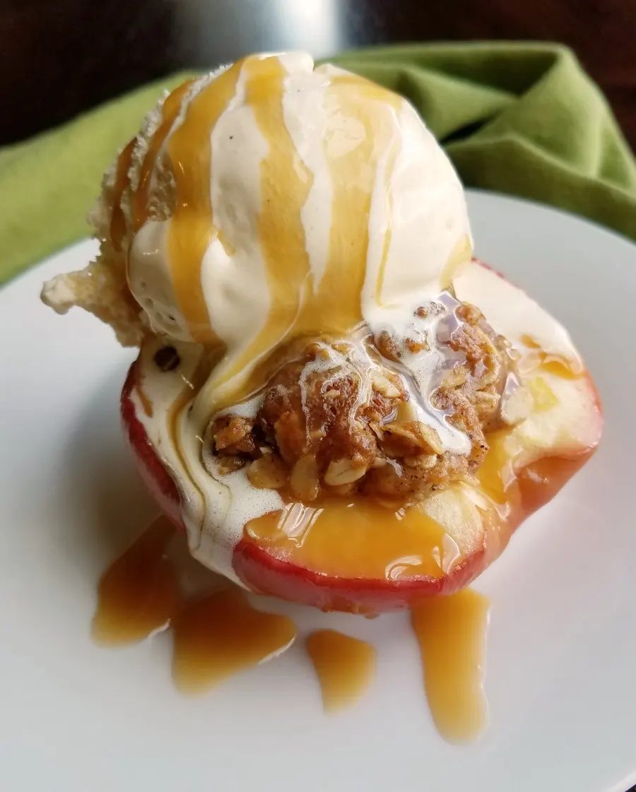 Baked apple half with brown sugar and oat filling topped with scoop of vanilla ice cream and drizzle of caramel sauce.