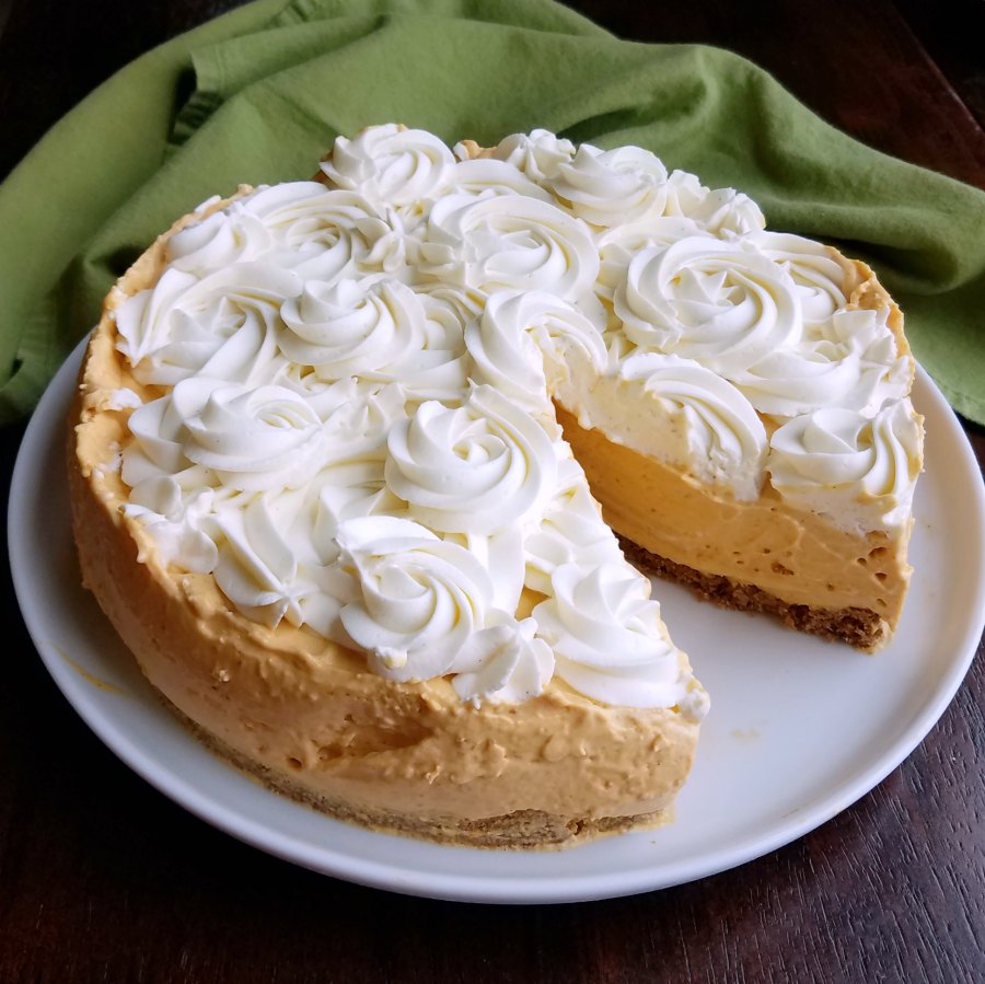 No bake pumpkin cheesecake topped with whipped cream swirls, missing a piece showing the creamy pumpkin layer beneath.
