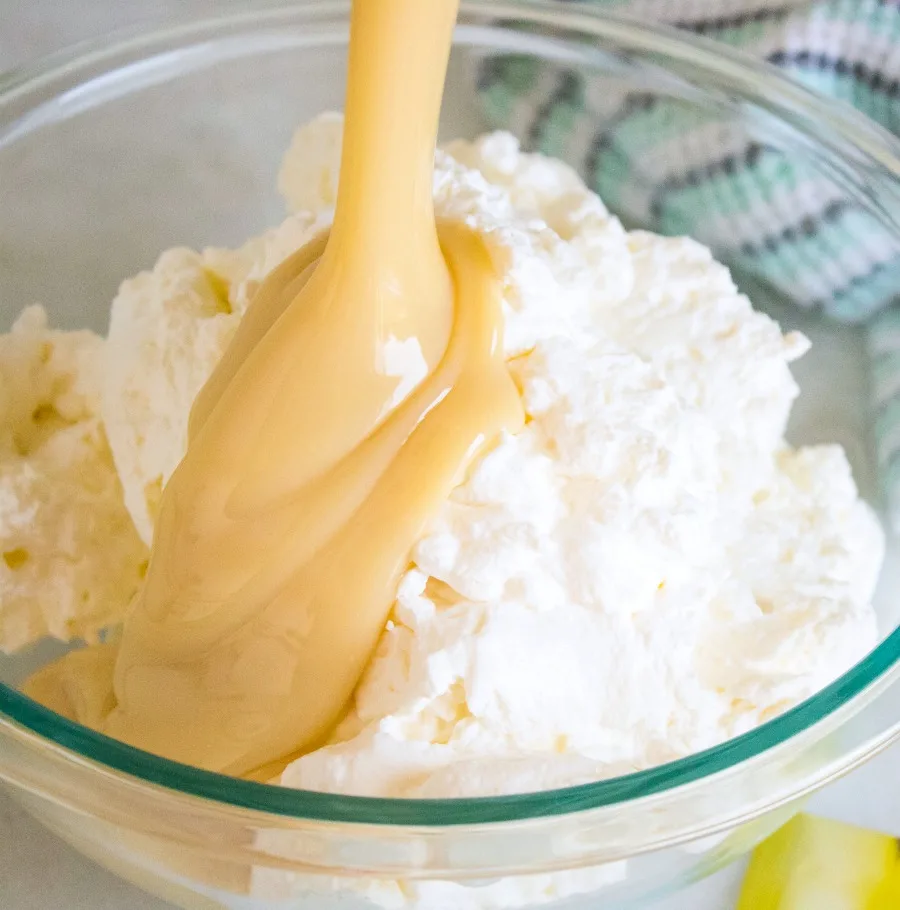 pouring sweetened condensed milk over whipped cream for no churn ice cream.