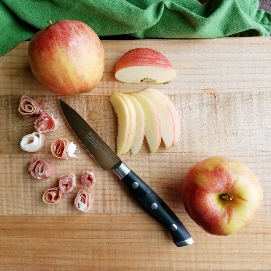 Slicing prosciutto into roses and apples into slices with paring knife. 