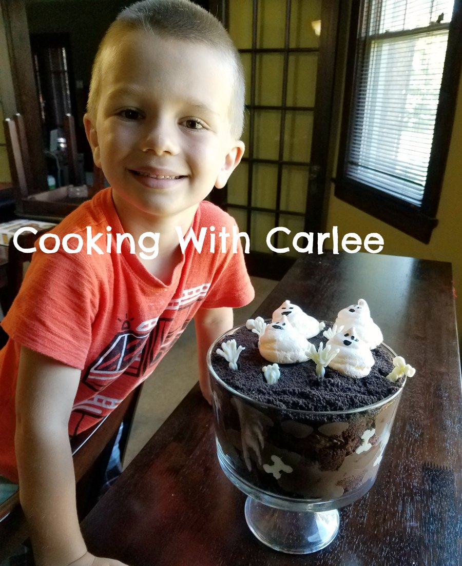Little Dude next to a glass trifle bowl filled with chocolate pudding, chocolate cake, white chocolate bones, and meringues ghosts.