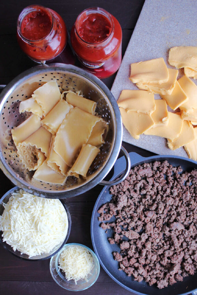 Ingredients for lasagna including pasta, sauce, velveeta slices, ground beef, mozzarella and parmesan.