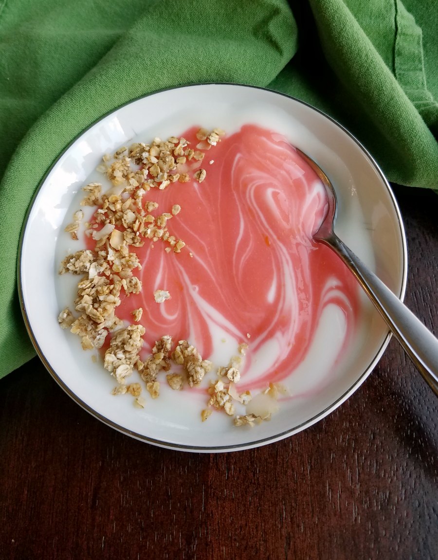 swirl of pink blood orange curd in yogurt with sprinkling of granola 