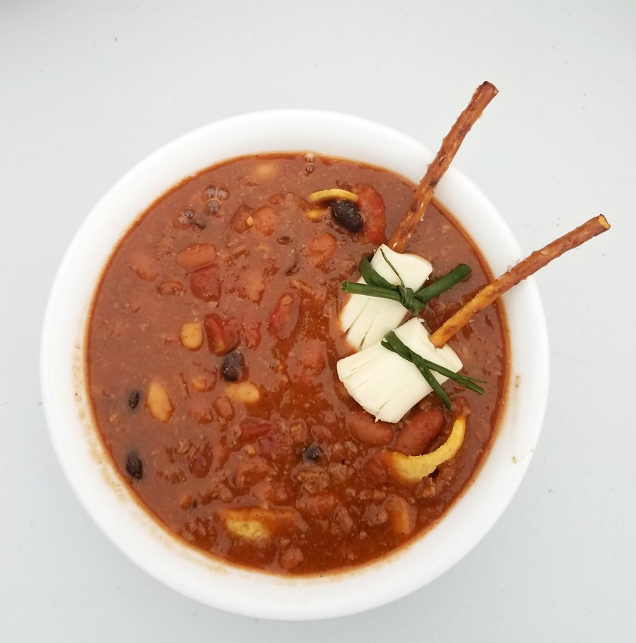 bowl of chili with cheese and pretzel broomsticks.