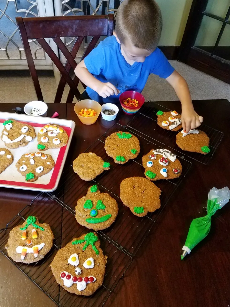 kid decorating pumpkin cookies with frosting and candy
