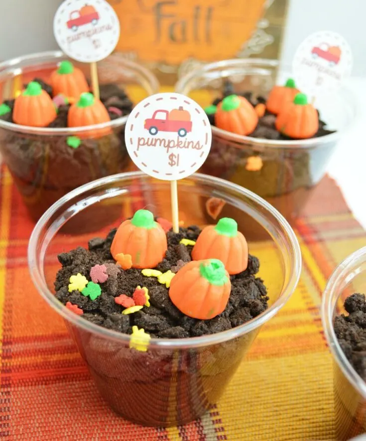 Small clear plastic cups filled with chocolate dirt pudding and topped with leaf sprinkles and pumpkin candies.