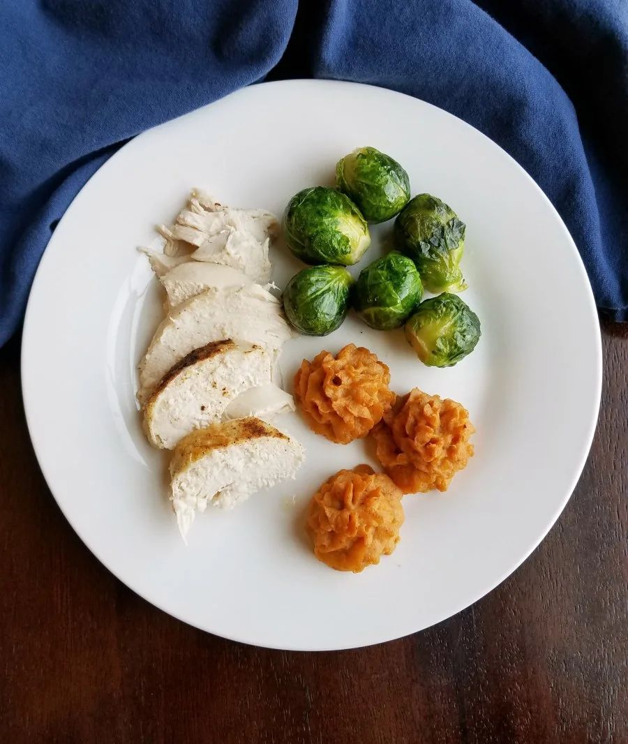 looking down on round dinner plate with duchess sweet potatoes, turkey and roasted brussels sprouts.