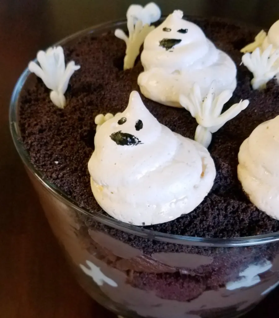 layers of chocolate in glass trifle bowl with white chocolate hands and meringue ghosts on top.
