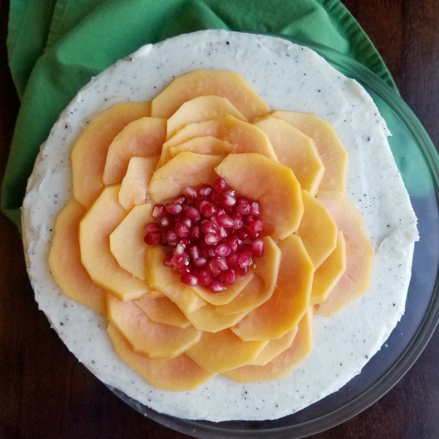 cake with white frosting specked with dragonfruit seeds and a papaya and pomegranate seed flower on top.