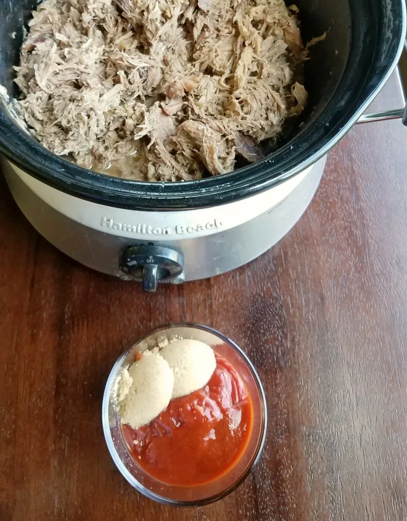 slow cooker filled with pulled pork with bowl of ingredients for sriracha sauce. 