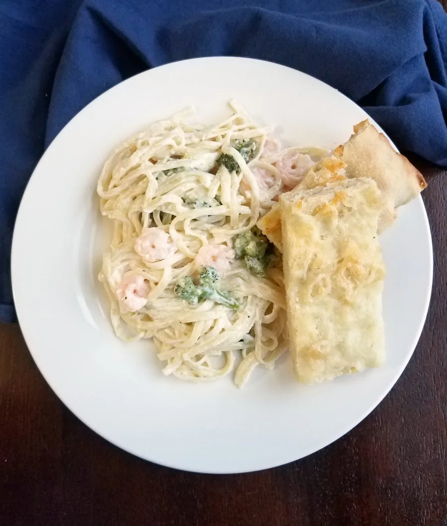 shrimp and broccoli fettuccine alfredo and slices of foccacia on plate.