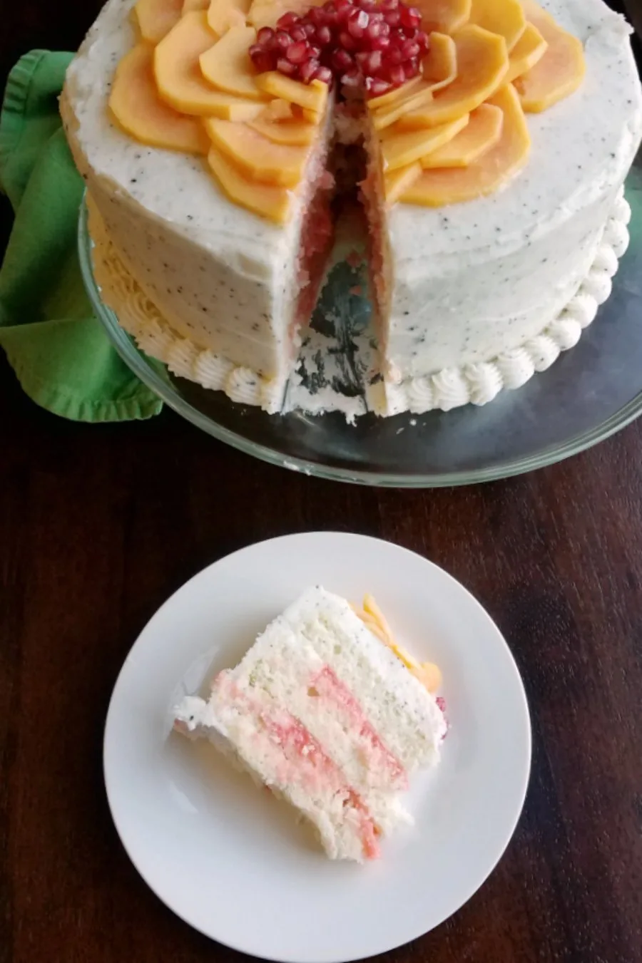 Slice of layered white cake with blood orange curd filling, and dragonfruit buttercream on plate, ready to eat, with remaining cake in the background.