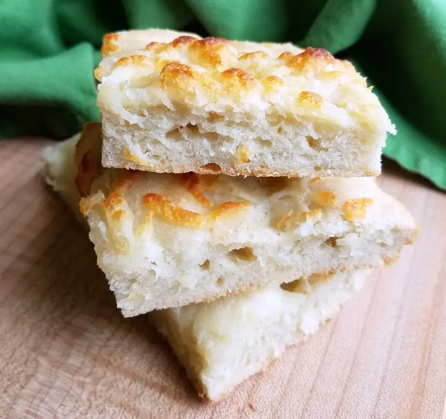 3 squares of cheesy garlic foccacia stacked on top of each other showing airy bread texture and golden brown cheese on top.