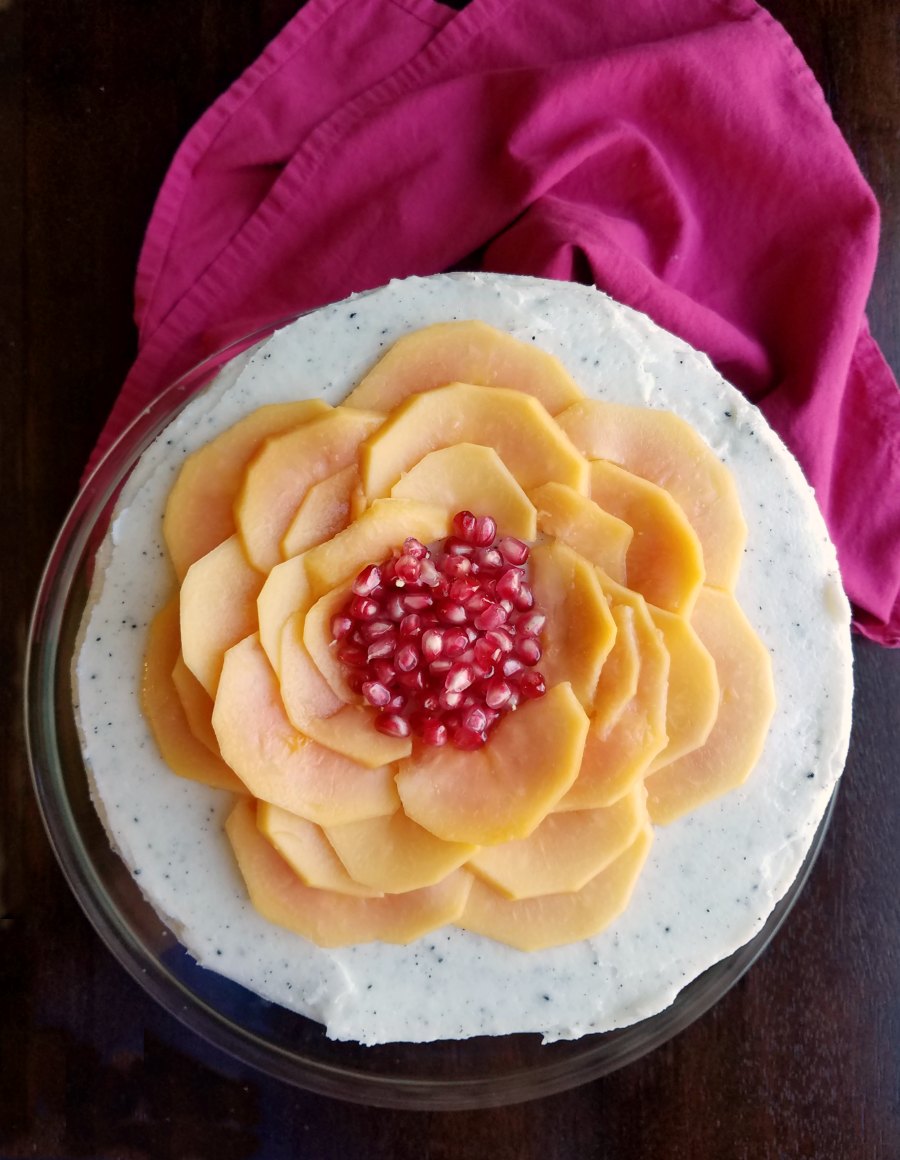 Looking down on round cake with speckled buttercream frosting with dragonfruit seeds and topped with sliced papaya and pomegranate seeds arranged to look like a large flower.