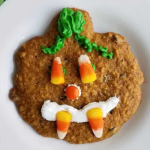 pumpkin shaped cookie with candy and frosting decoration to look like a jack-o-lantern.
