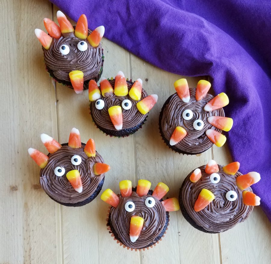Selection of cupcakes with chocolate frosting decorated to look like turkeys with candy eyes and candy corn.