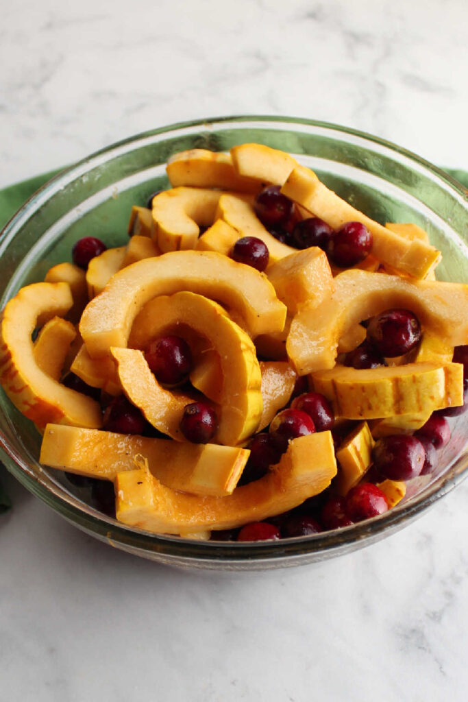 Bowl of sliced delicata squash and fresh cranberries ready to be tossed in honey and spices.
