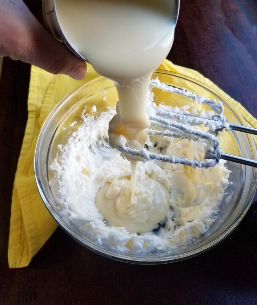 pouring cold sweetened condensed milk over bowl of whipped butter.