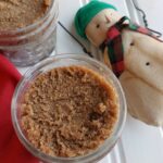 Jars of homemade snickerdoodle brown sugar scrub with a snowman decoration nearby.