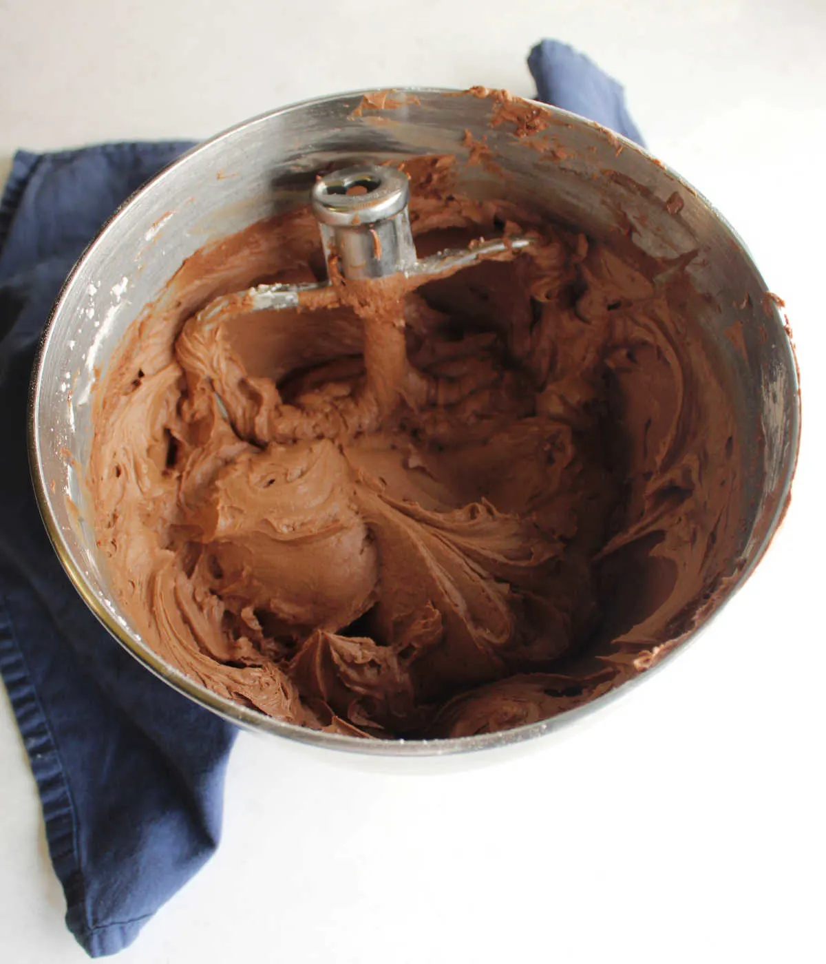 Mixer bowl filled with chocolate fudge frosting and mixer paddle showing creamy chocolate texture.