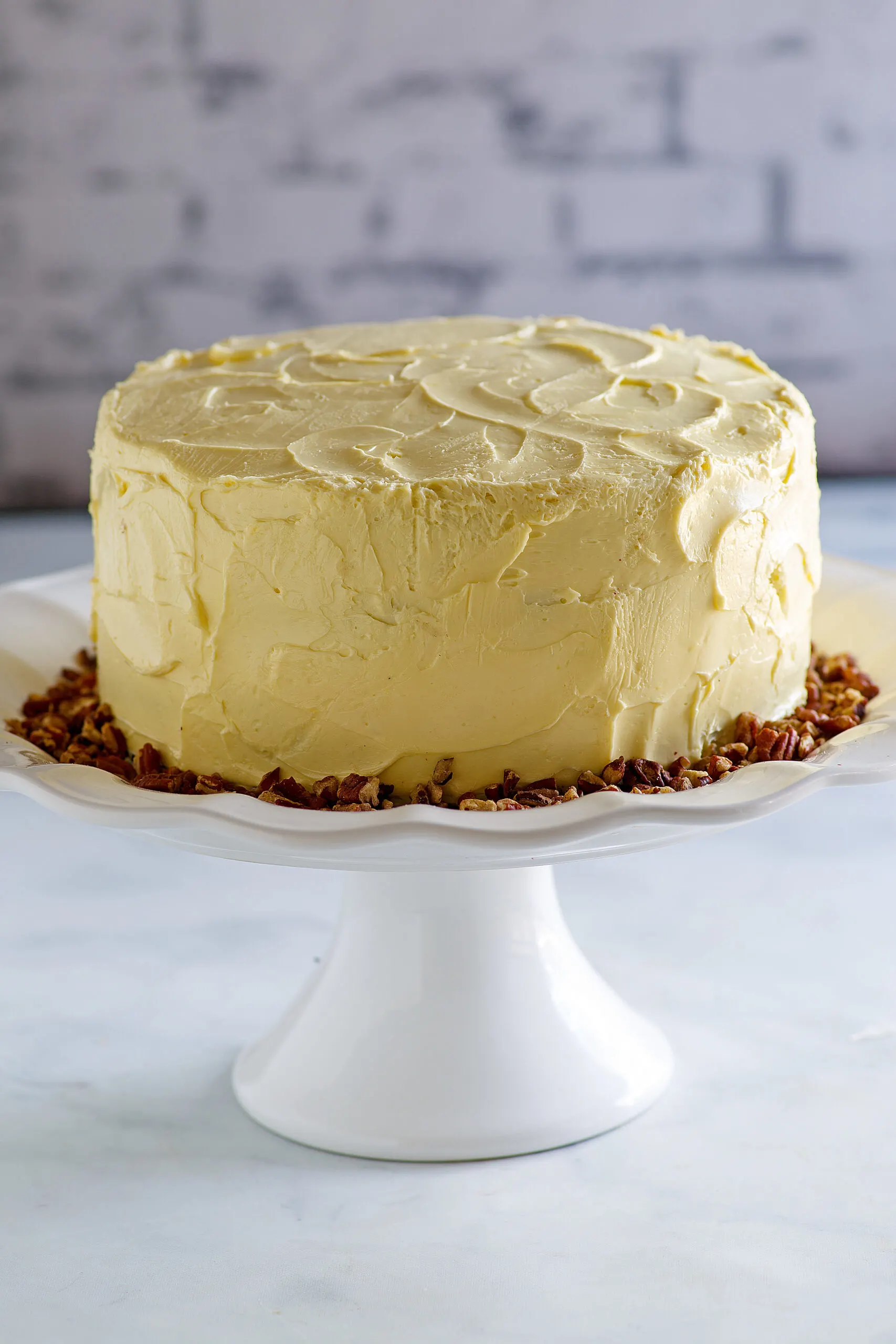 maple frosted layer cake with pecans on white cake stand