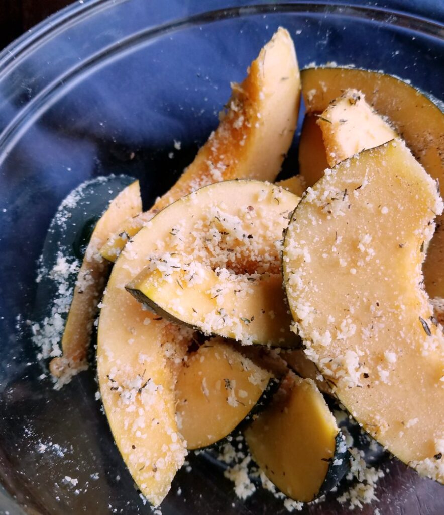 bowl full of raw acorn squash tossed with parmesan cheese and herbs ready to go in air fryer.