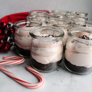 Jars of peppermint no bake cheesecake with chocolate crust and candy cane filling ready to eat.