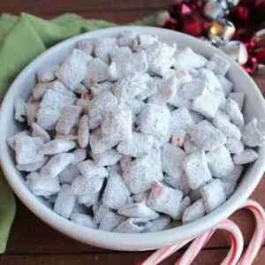 Close up of a bowl of dark chocolate peppermint muddy buddies coated in powdered sugar and candy canes, ready to eat.