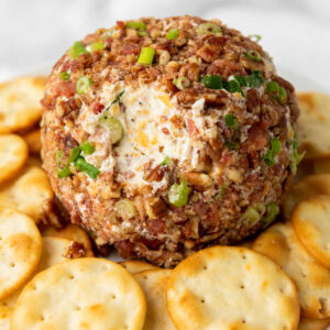 Cheddar bacon ranch cheese ball coated in green onions and pecans with a little bit missing showing the cheesy inside.