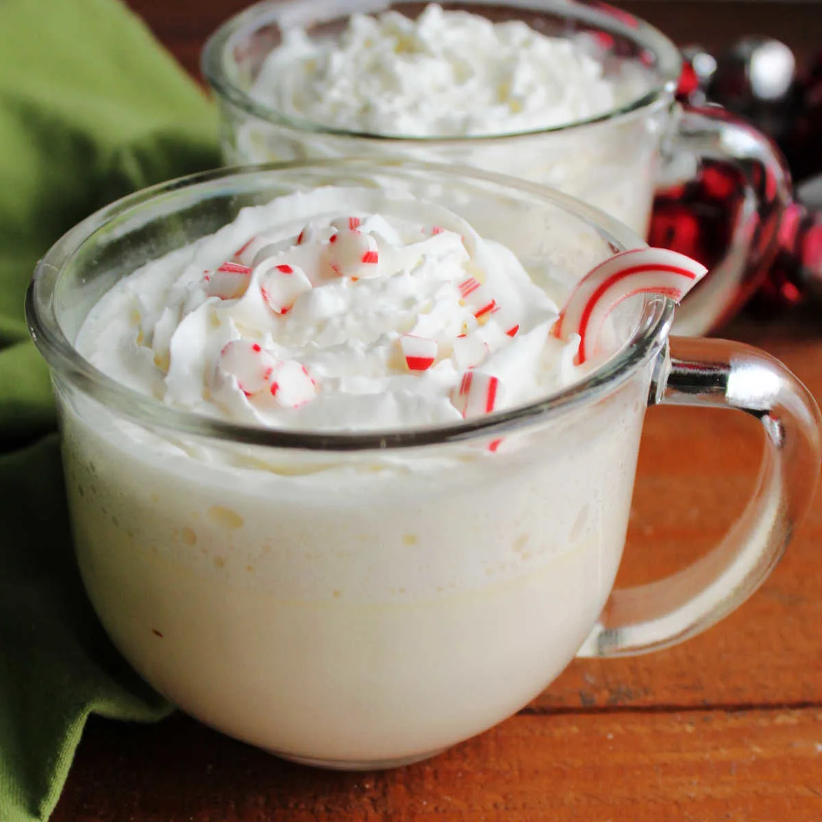 Two large glass mugs filled with creamy peppermint white hot chocolate topped with whipped cream and candy cane pieces.
