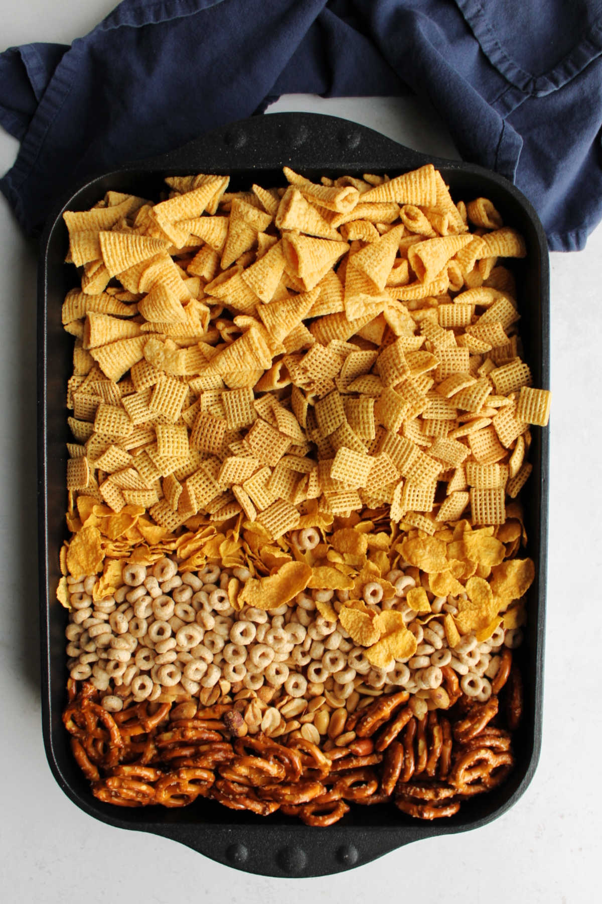 Pan filled with bugles, pretzels, Chex, peanuts, cornflakes and Cheerios ready to be coated in caramel mixture for caramel chex mix. 
