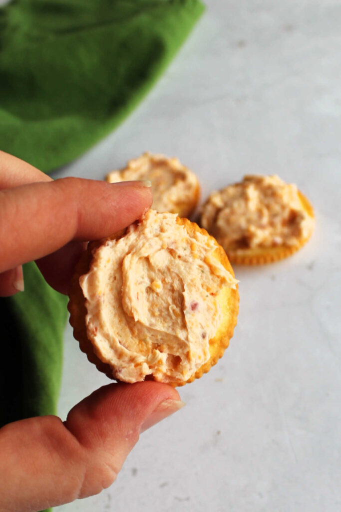 Hand holding cracker with bacon cheese ball spread on it.