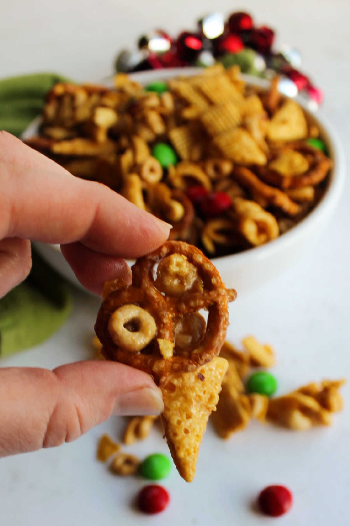 Hand holding a cluster of cheerios, a pretzel and a bugle all held together with a crunchy caramel mixture.