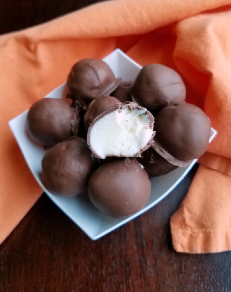 Bowl of chocolate coated truffles with one cut in half on top showing the white orange flavored cream cheese center. 