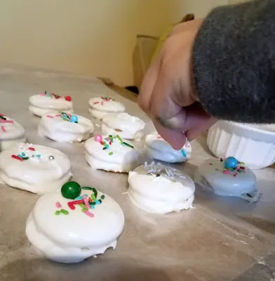 child's hand applying sprinkles to freshly dipped white chocolate coated fluffernutter cracker sandwich cookies