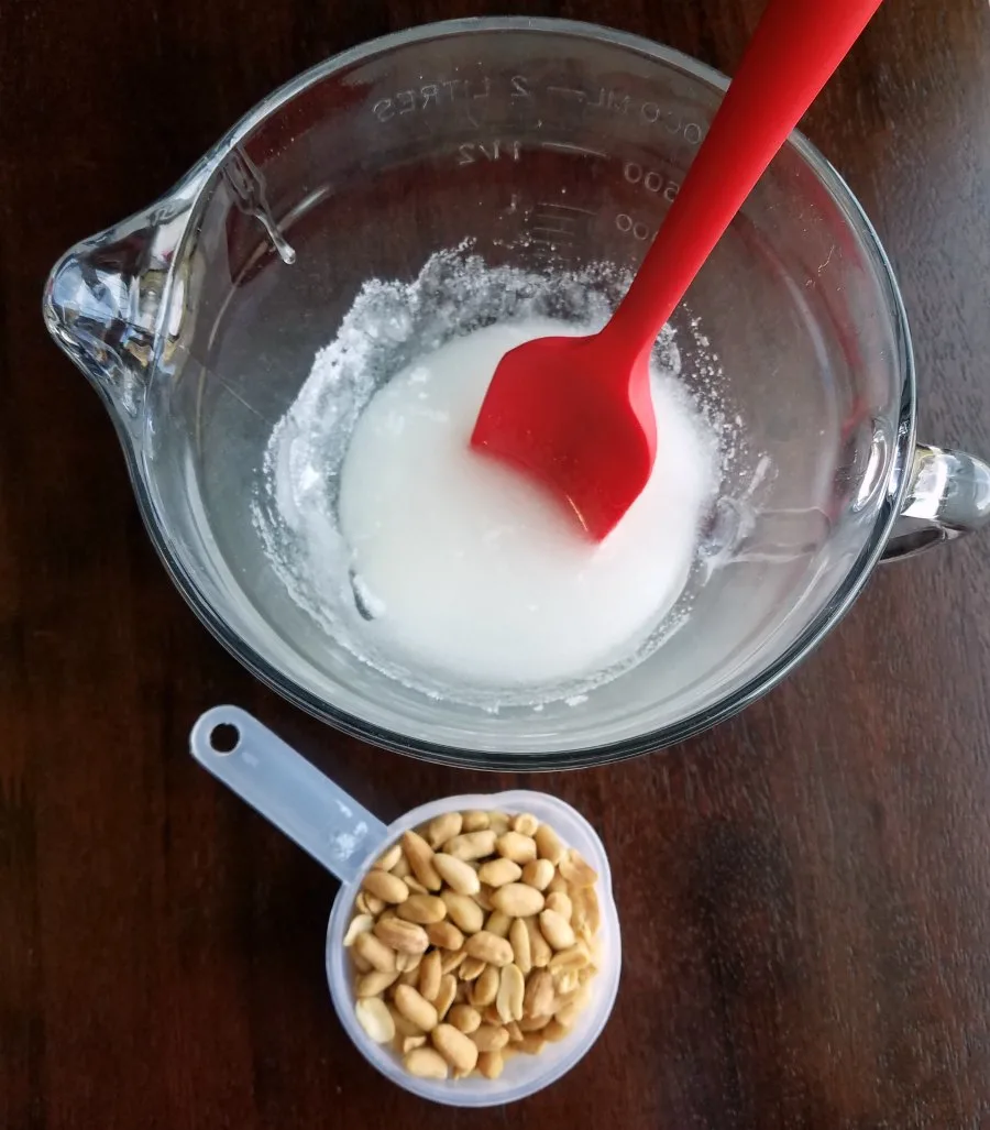 sugar mixture in glass bowl by measuring cup of peanuts.