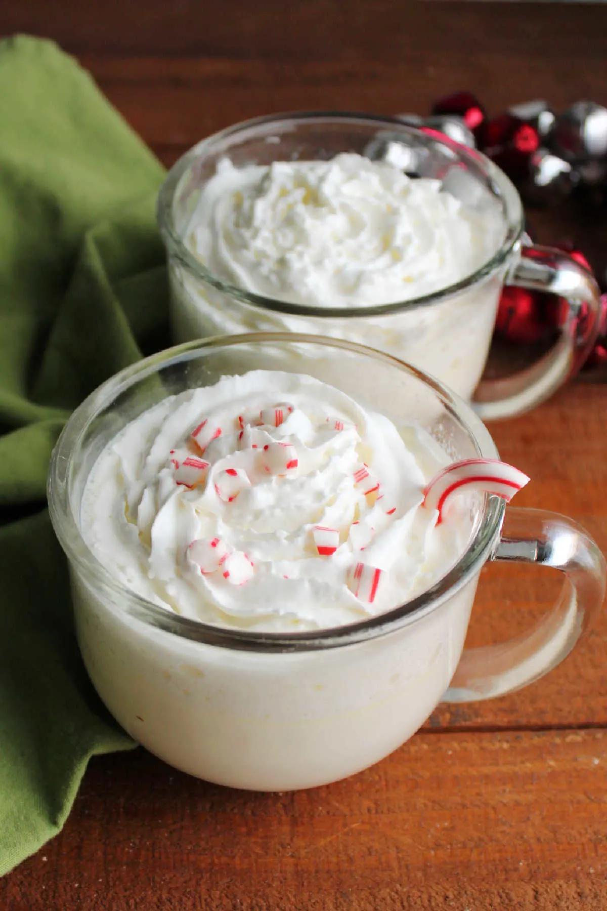 Mugs of white hot chocolate topped with whipped cream and candy cane bits. 