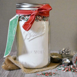 Glass jar filled with sugar cookie mix and sprinkles with gift tag.