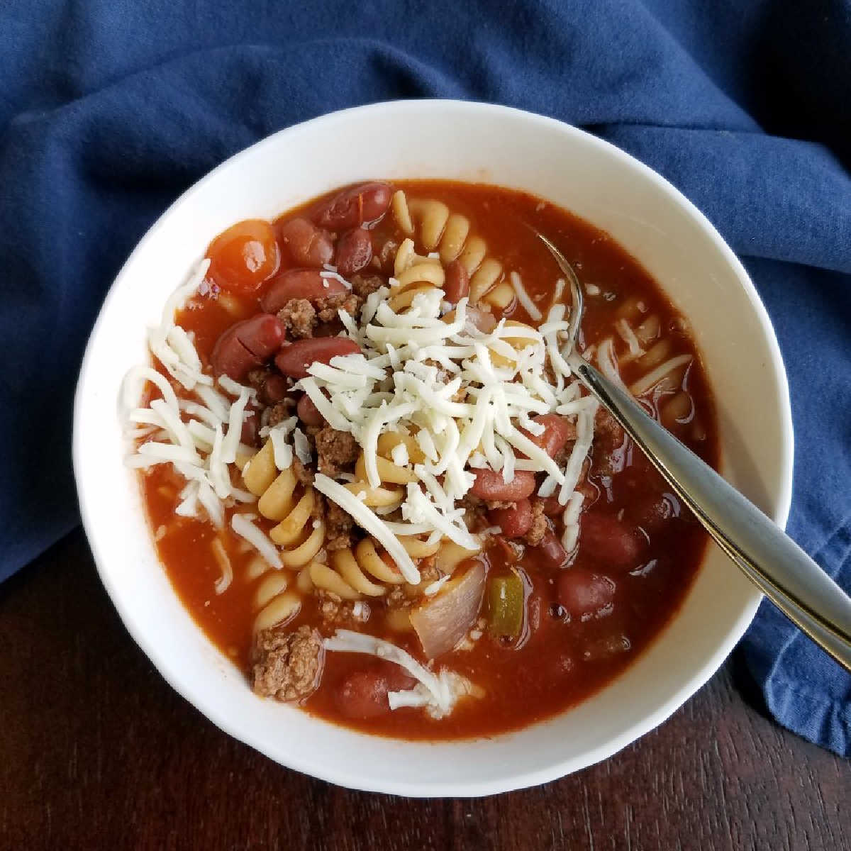 bowl of chili soup with pasta in it and cheese on top.