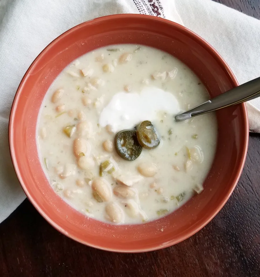 Bowl of creamy white chicken chili topped with sour cream and pickled jalapeno slices, ready to eat.